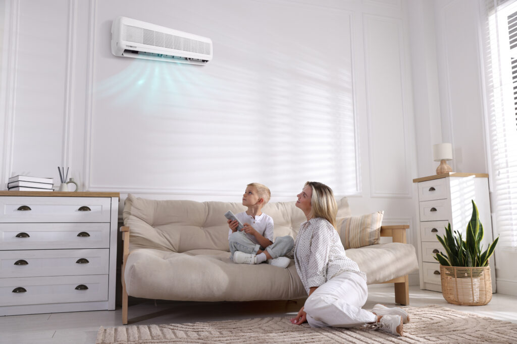 Woman and her son using remote to control air conditioner on sofa at home