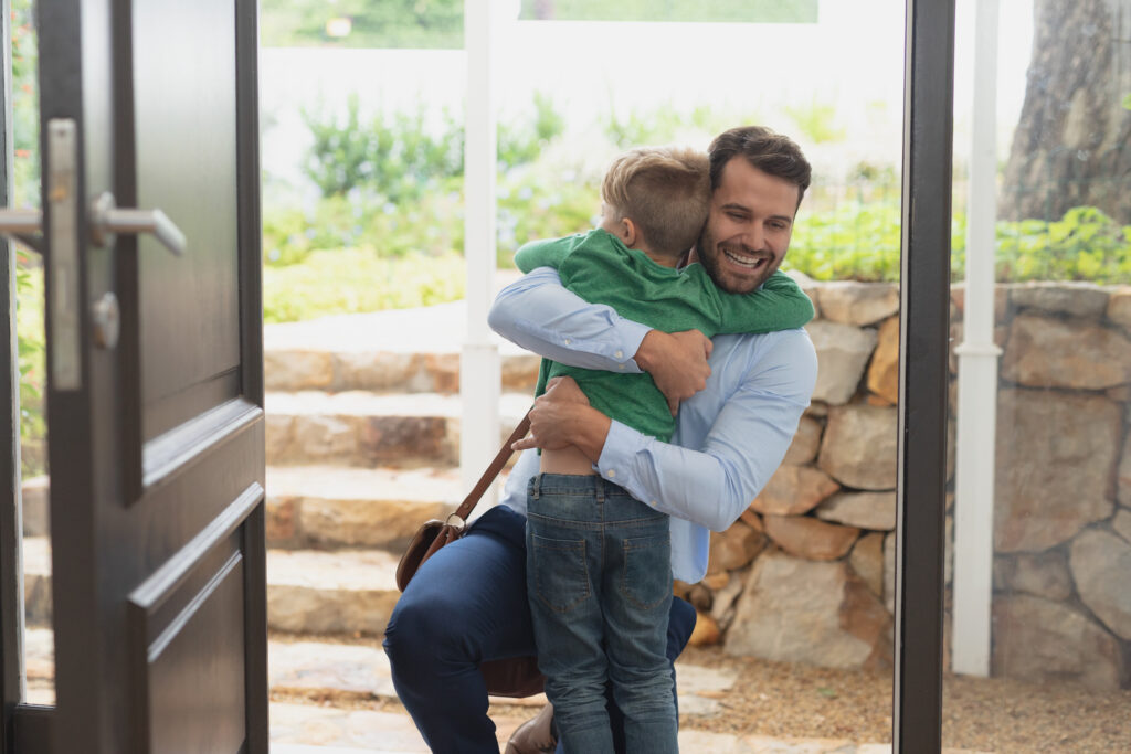 Front view of happy Caucasian father embracing his son as he enters the house